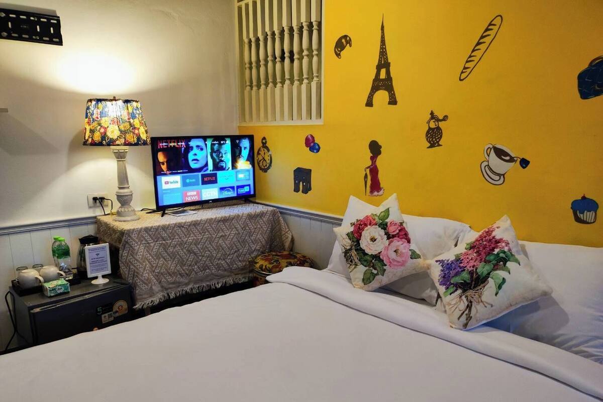 A hotel room with a bed, a TV displaying Netflix, and a wall decorated with Eiffel Tower and other icons.