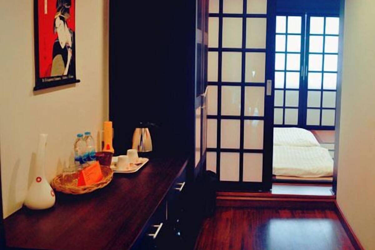 A hotel room with a wooden desk, a framed picture, a sliding door with a view, and a bed with a white comforter.