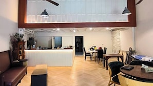 Ein geräumiger Raum mit hoher Decke, Holzbalken, einer zentralen Barinsel, einem Essbereich mit Stühlen und Tisch sowie einer Sitzecke mit Sofa und kleinem Tisch.
