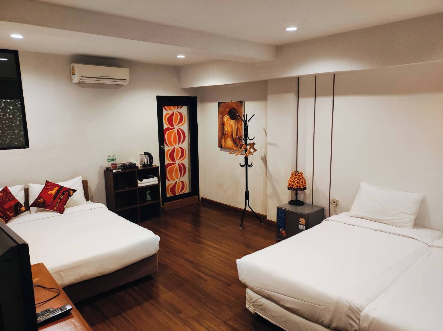 A hotel room with two beds, a wardrobe, a desk with a lamp, and a painting on the wall.