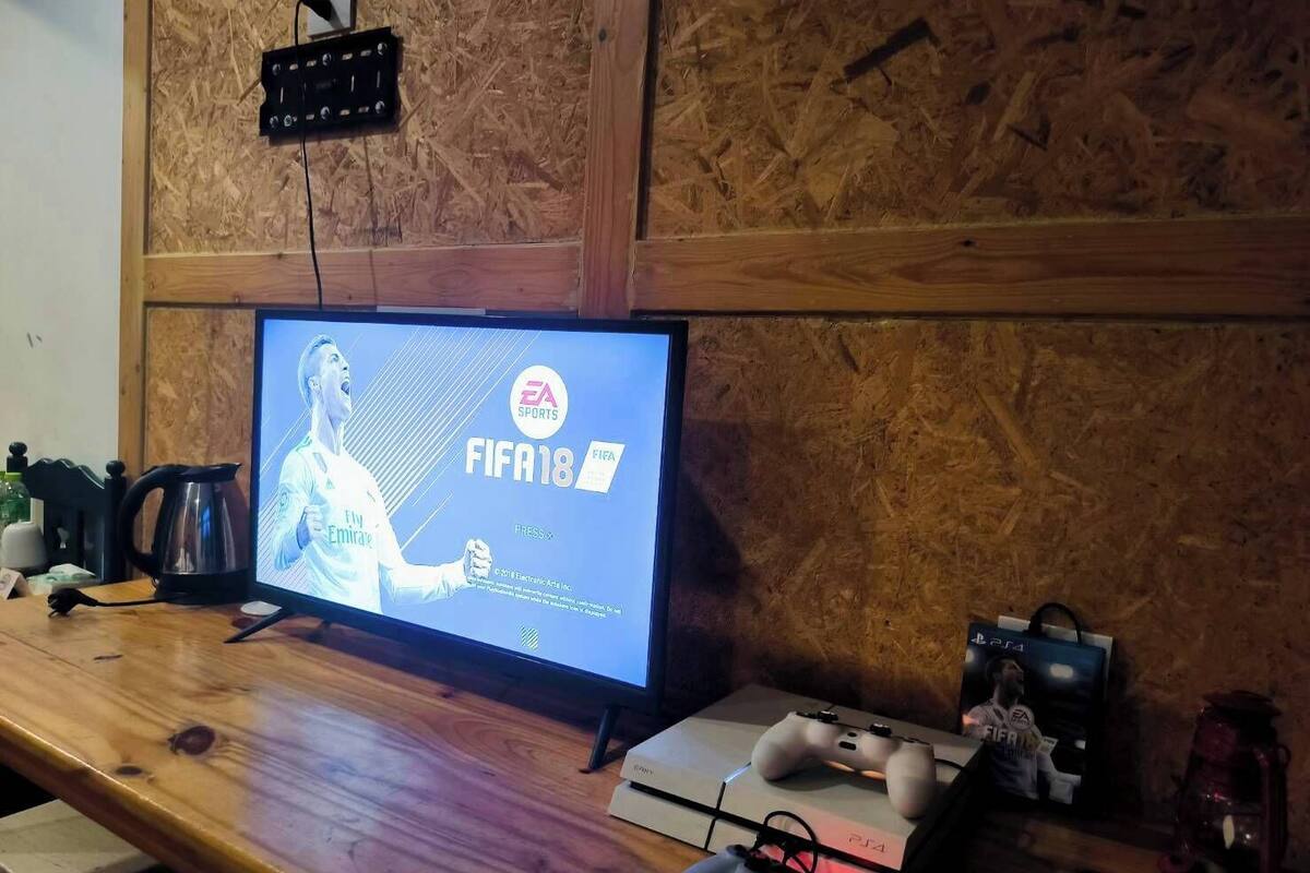 A wooden table with a PS4 and a PS4 Pro, a TV displaying FIFA 18, and a PS4 controller.