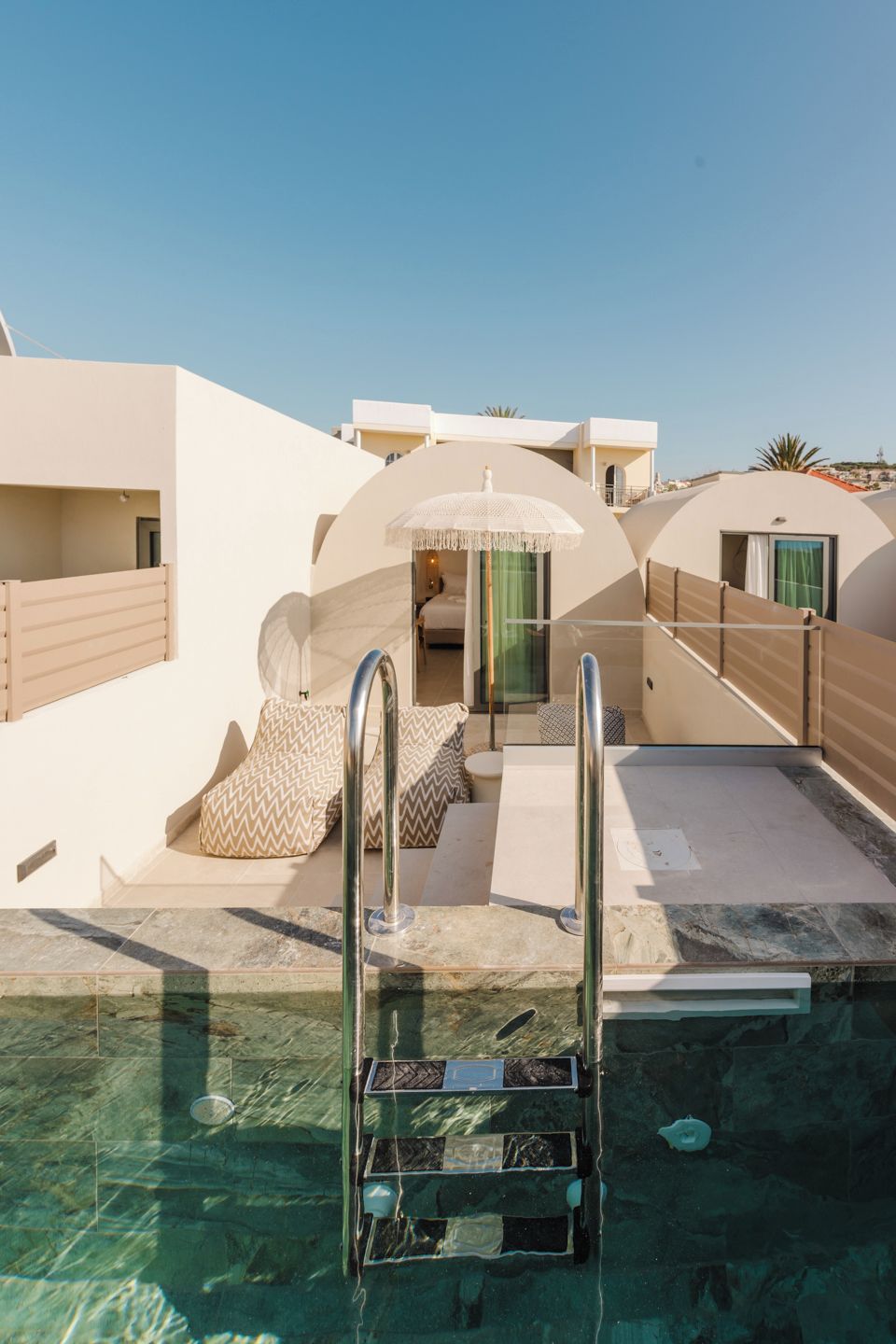 Een zwembadgedeelte met een helder zicht op het zwembad, een trap die het water in leidt, en een terras met zitplaatsen en een glazen deur naar een kamer.