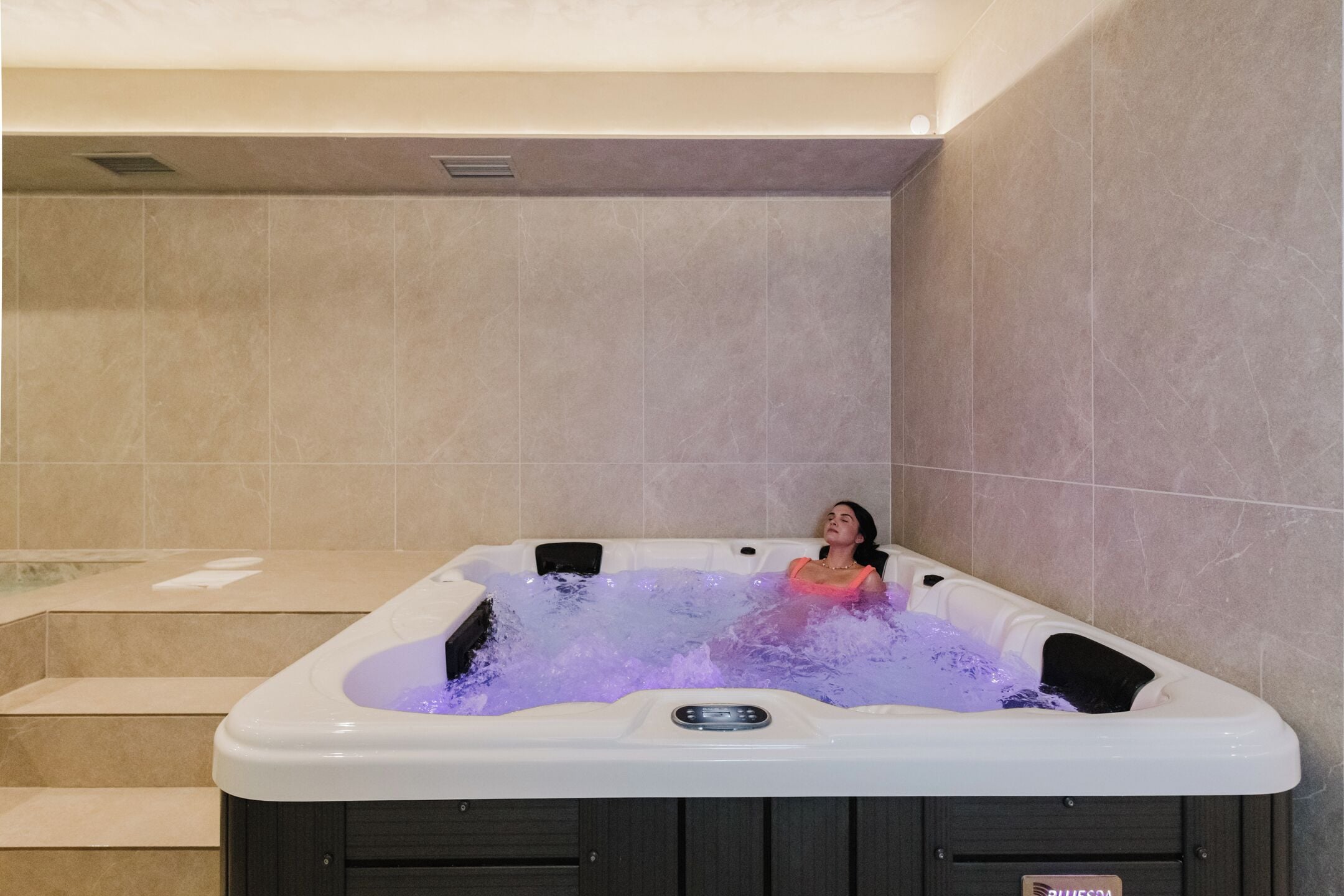 A hot tub with a person inside, surrounded by tiled walls and steps.