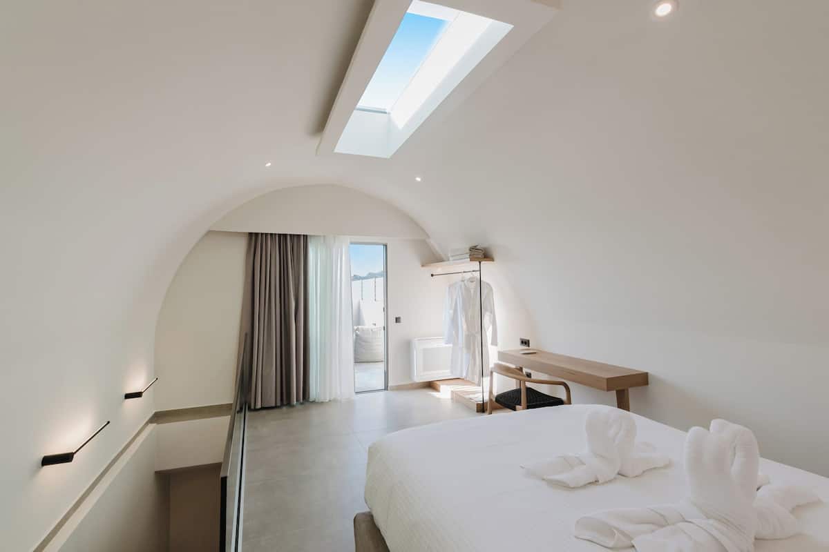 A modern hotel room with a skylight, a bed with towels, a desk, and a view of the outdoors.