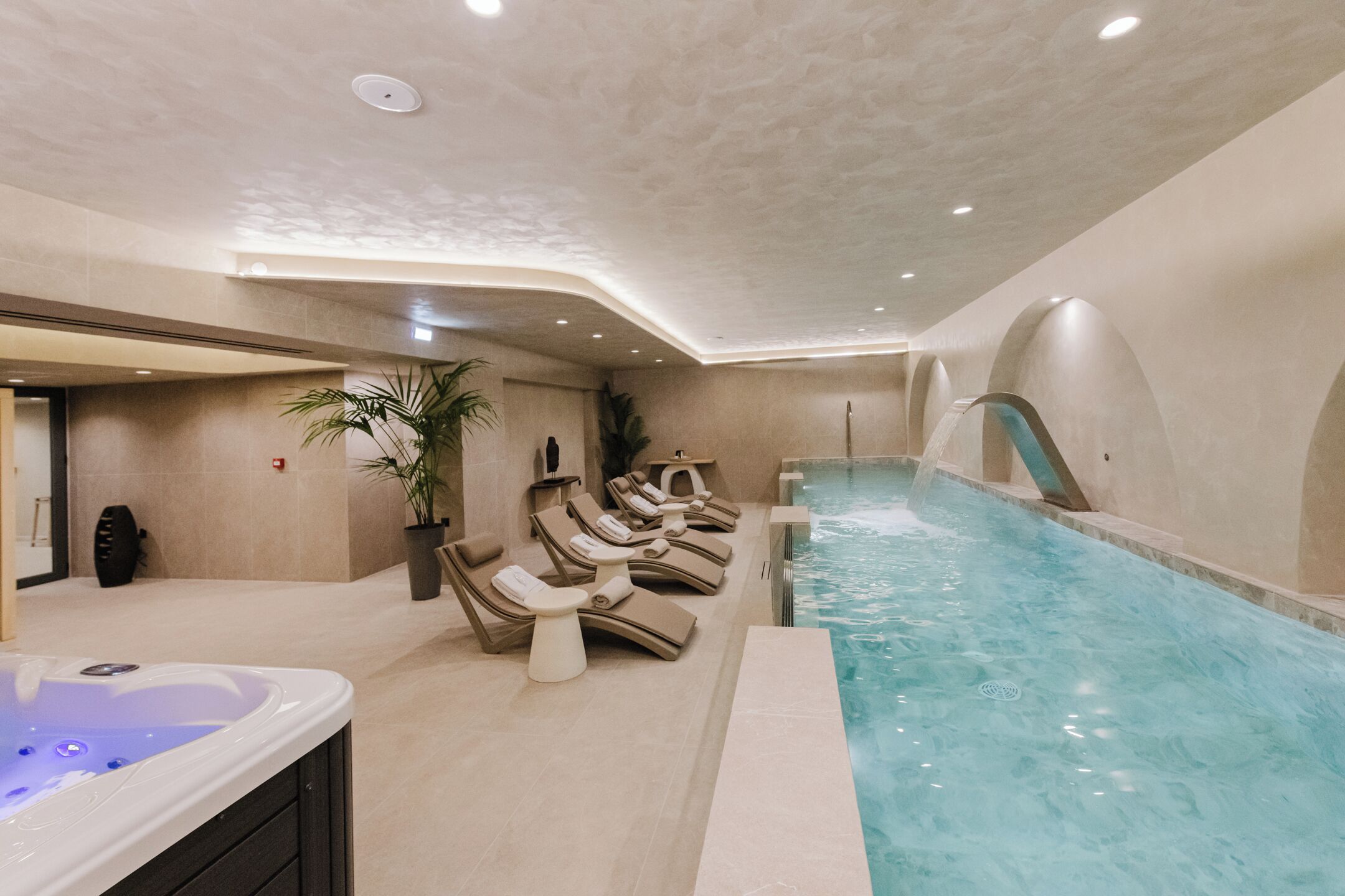 Un espace piscine intérieur moderne, doté de chaises longues et d’un jacuzzi.