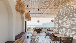 Un espacio para comer al aire libre con mobiliario de mimbre, vista al mar y techo de bambú.
