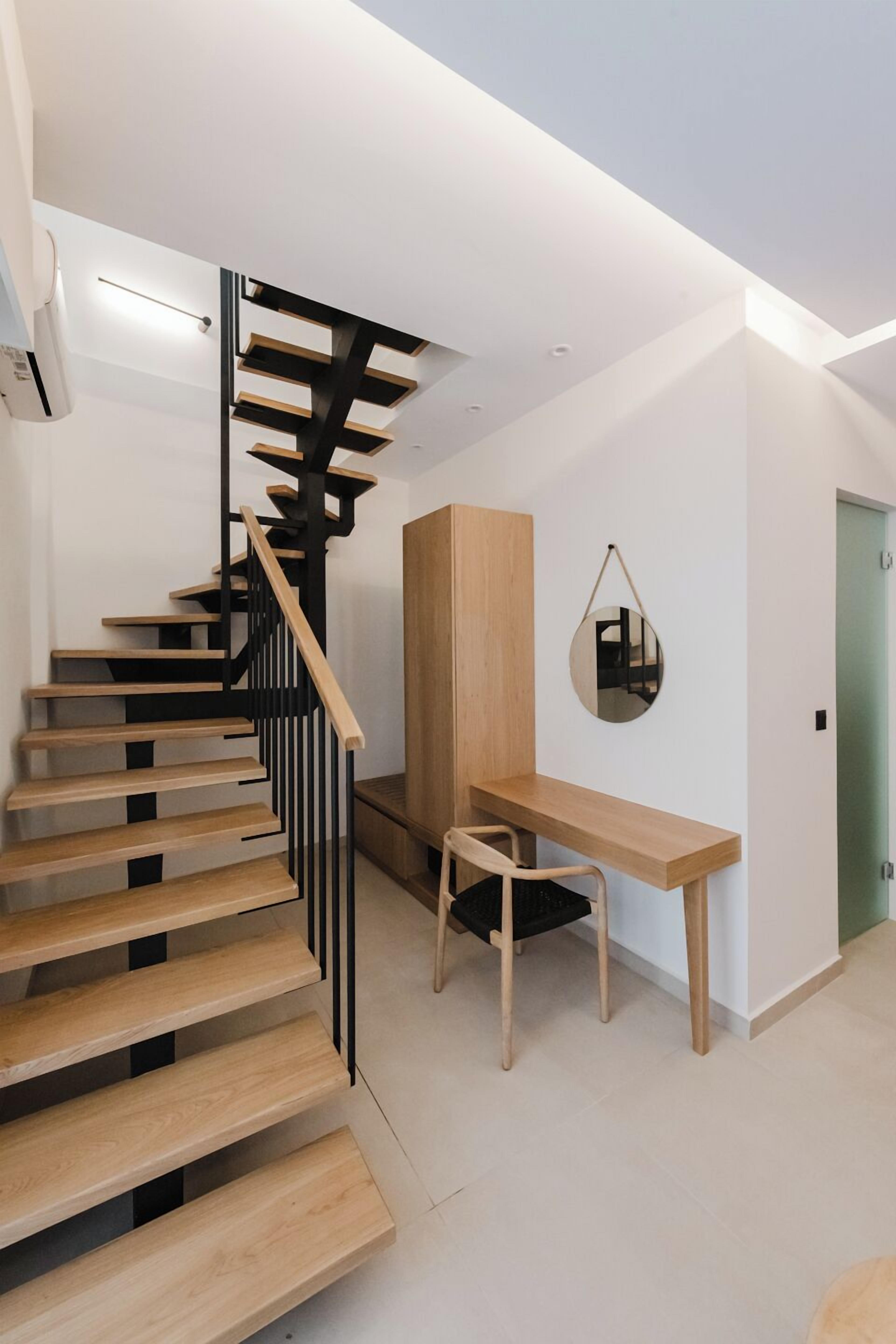 A modern staircase with wooden steps and black railings, a wooden desk with a chair, and a mirror on the wall.