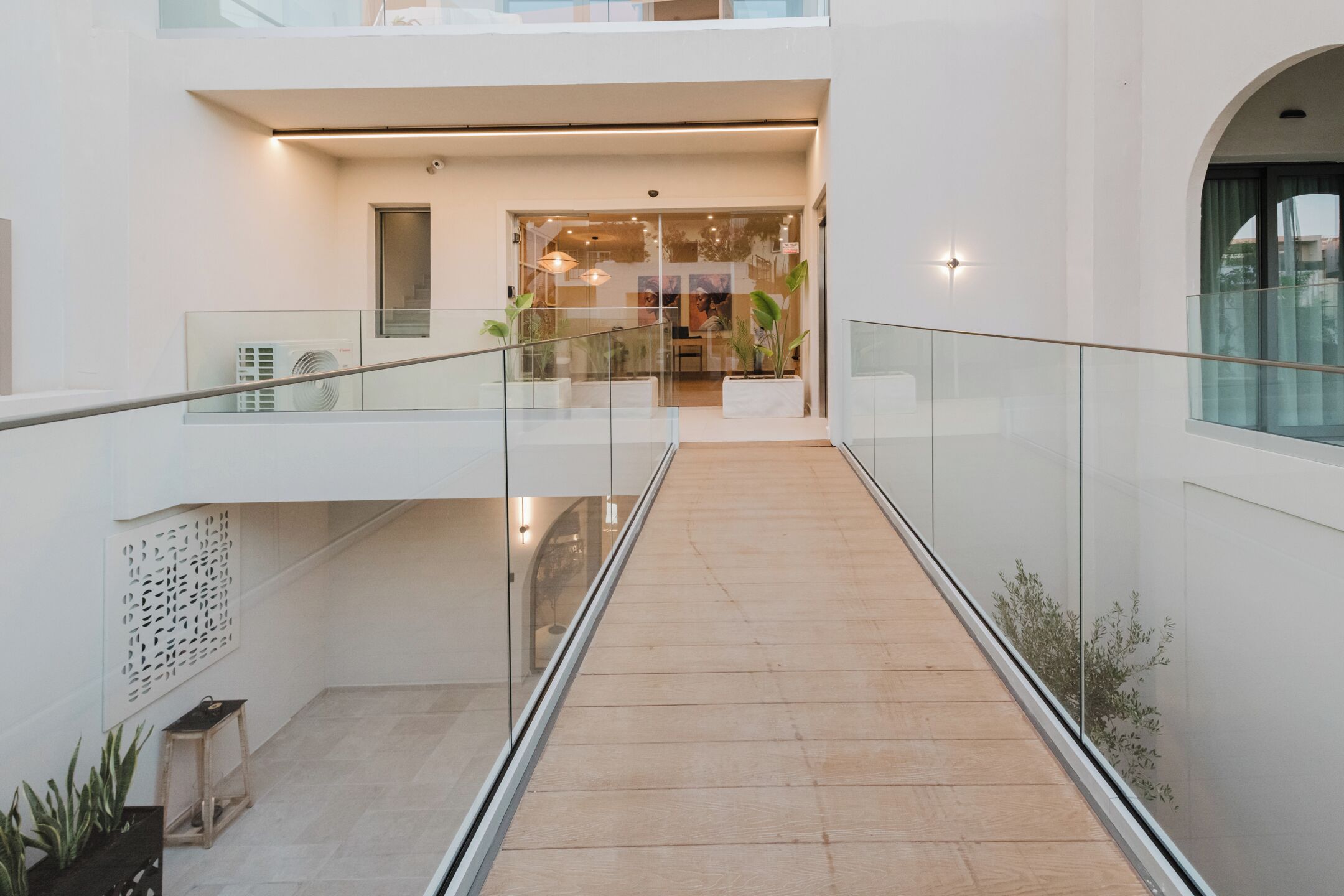 Un interior modern amb barana de vidre, sòl de fusta i vista cap a una zona de menjador.