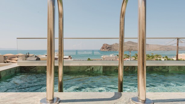 Una piscina con barandillas metálicas y vistas al mar y un puente al fondo.