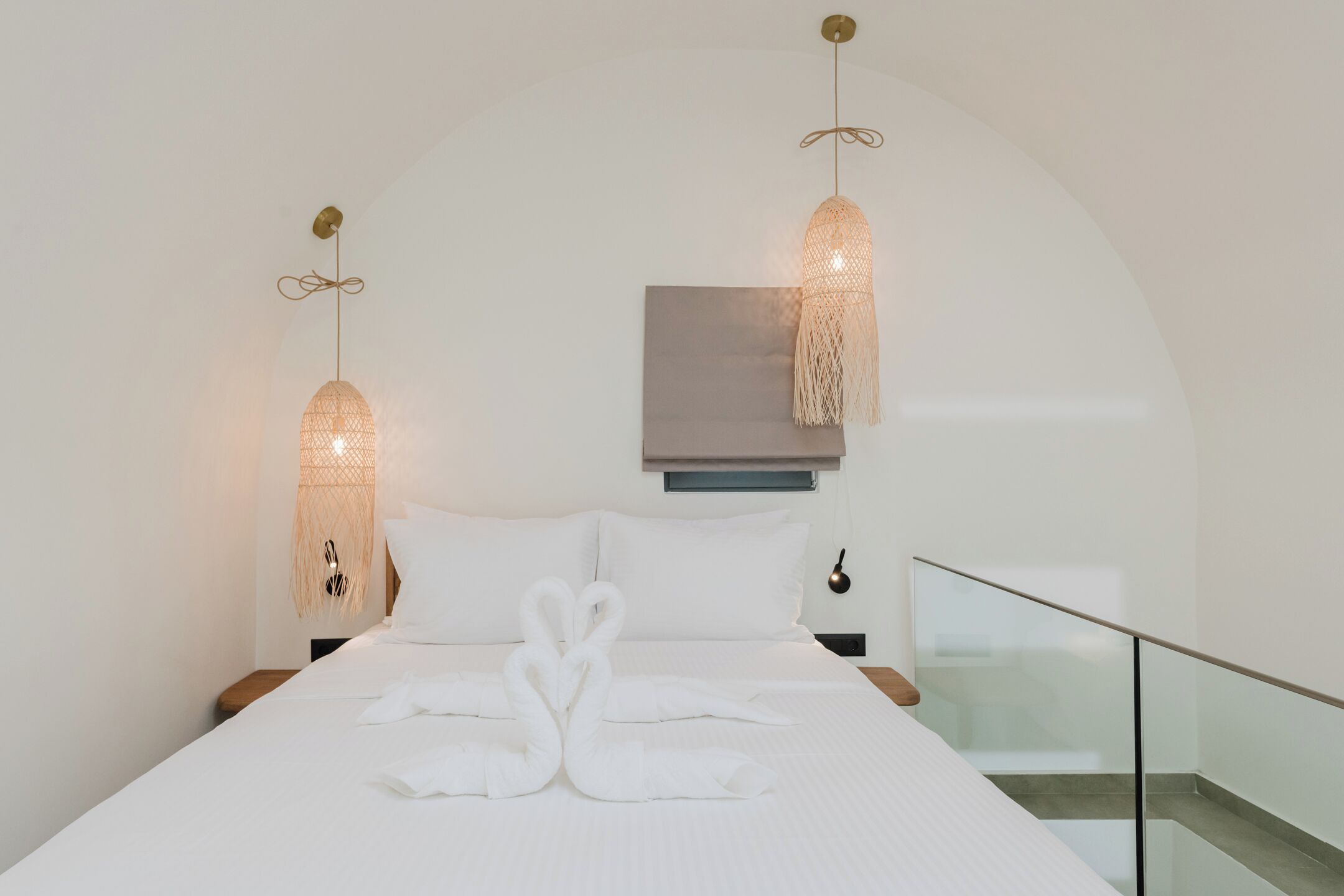 A modern hotel room with a large bed, two wall-mounted lamps, and a view of the balcony.