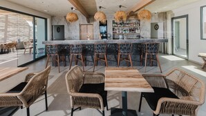 Un área de bar moderna con barra, sillas de mimbre y un espacio de estar con mesas y sillas.