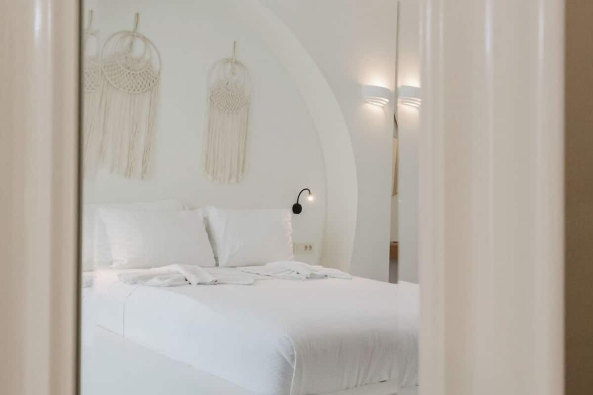 A modern bedroom with a large bed, white bedding, and wall-mounted macrame decorations.