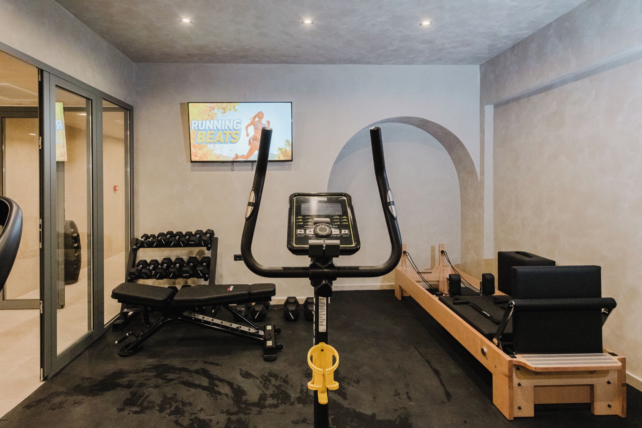 A home gym with cardio equipment, dumbbells, and a TV displaying a fitness program.