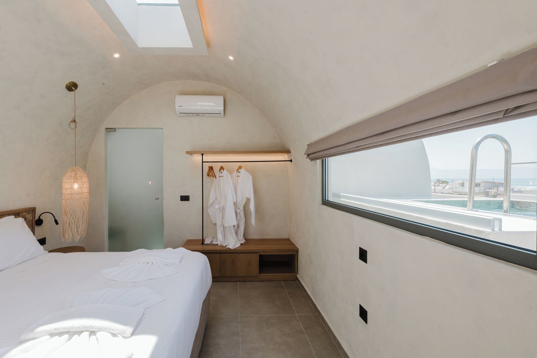A bedroom with a bed, a bench, a robe rack, and a window with a view of the city.