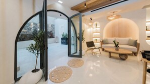 Una sala moderna con un sofá, una mesa de centro y una mesa de comedor. Hay una puerta de cristal que da a un espacio exterior con plantas.