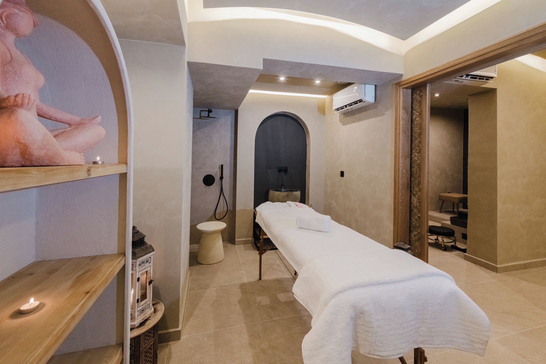 Un spa moderno con una camilla de masaje, un estante de madera con una vela y un aire acondicionado instalado en la pared.