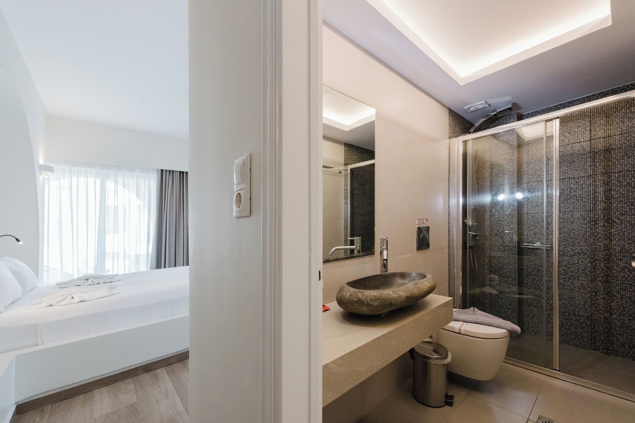 A modern bathroom with a stone sink, a glass shower enclosure, and a separate toilet.