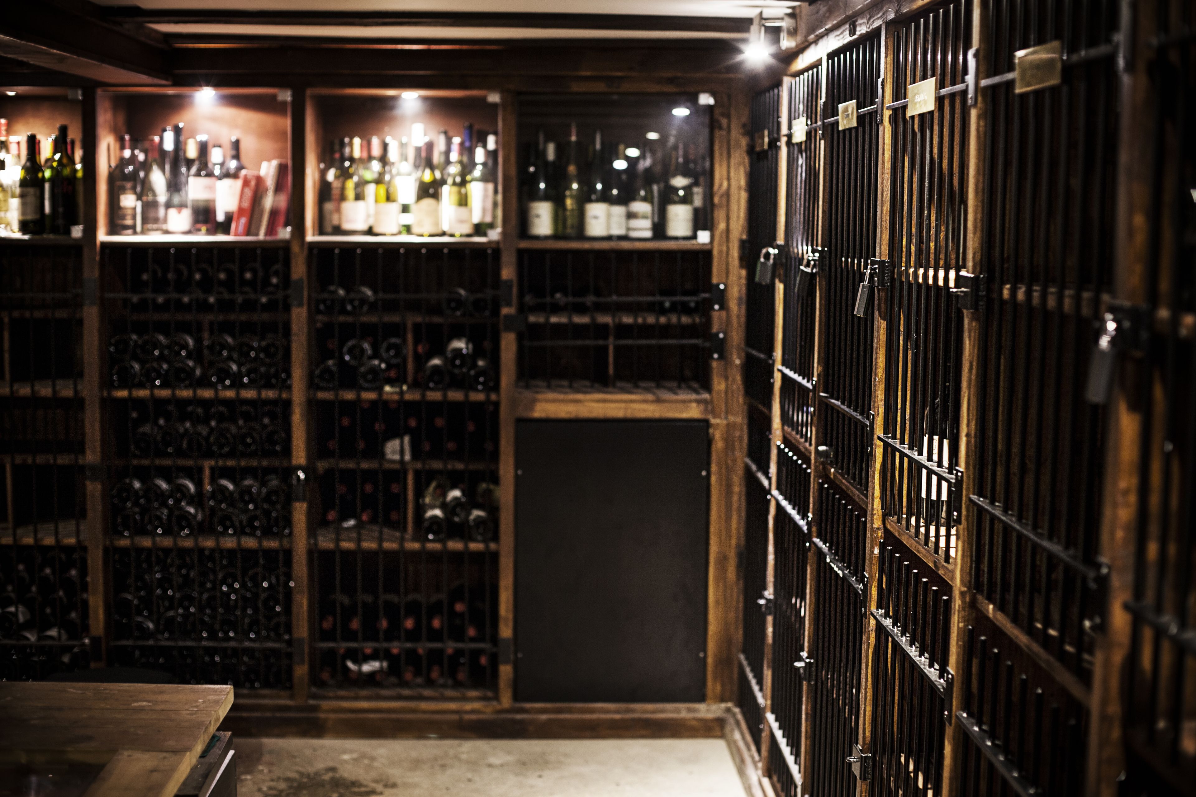 A wine cellar with wooden racks and metal cages holding wine bottles.