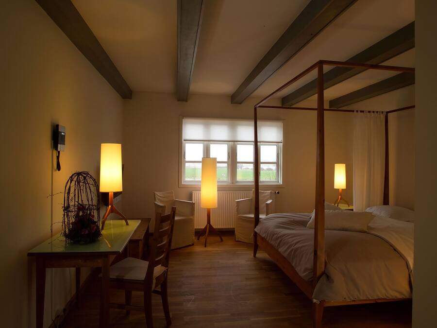 A four-poster bed, a desk with a lamp, a chair, and a window with blinds.