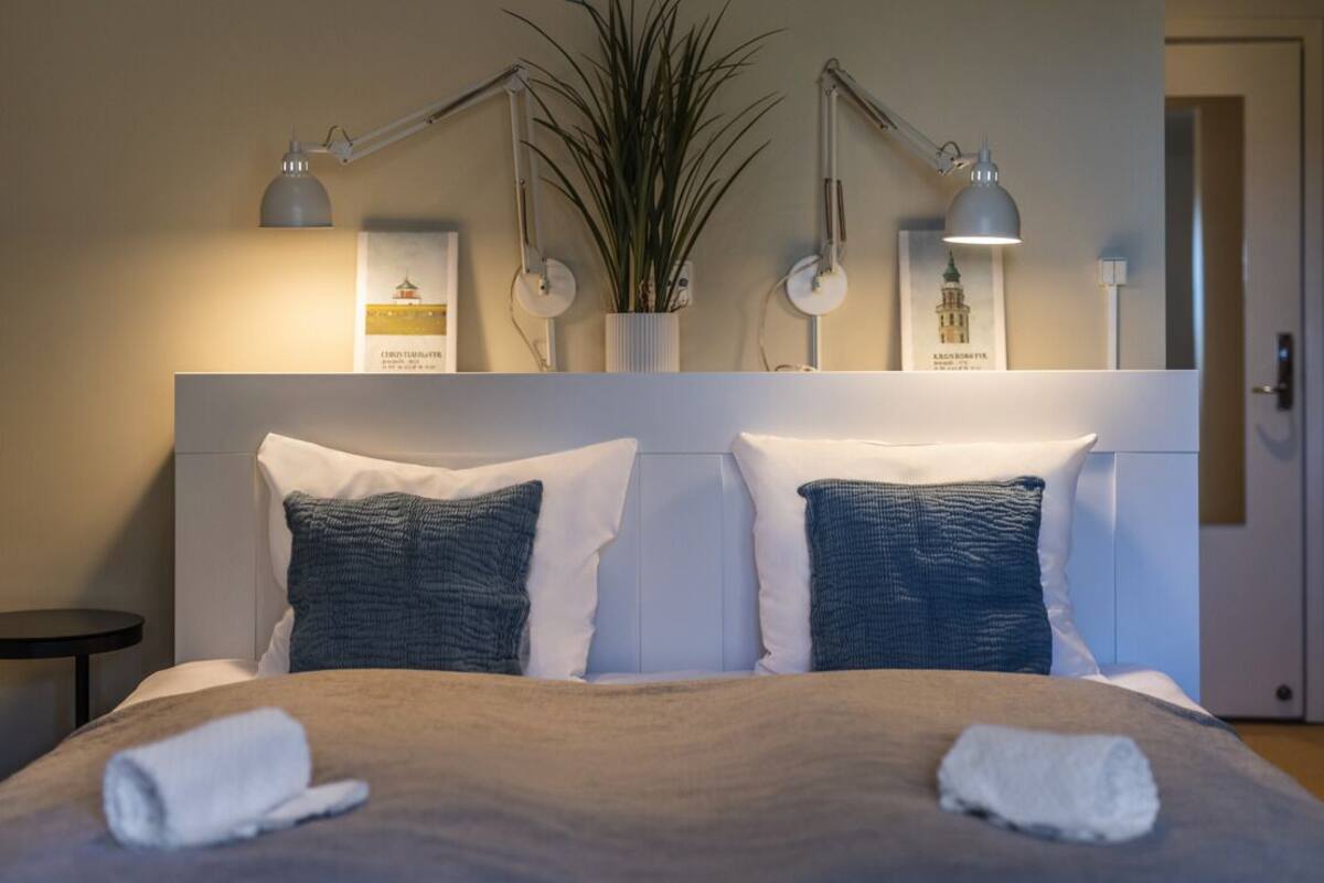 Una cama bien hecha con dos almohadas, una mesita de noche y lámparas de pared.