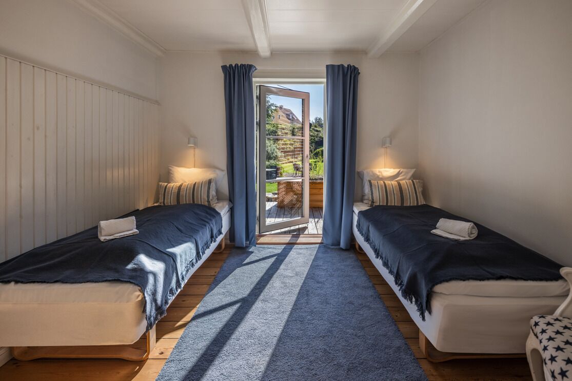 Un dormitorio con dos camas, una puerta corrediza de vidrio a un balcón y una alfombra azul.