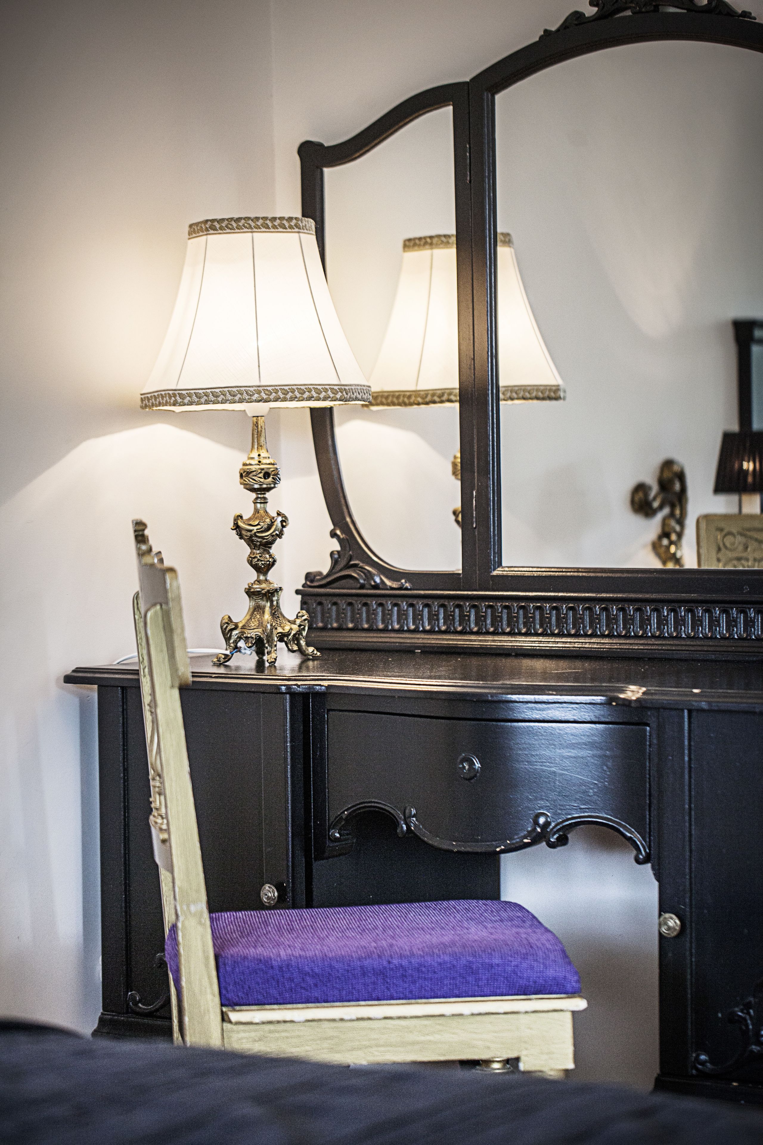 A room with a dark wooden dresser, a mirror, and a purple upholstered chair.