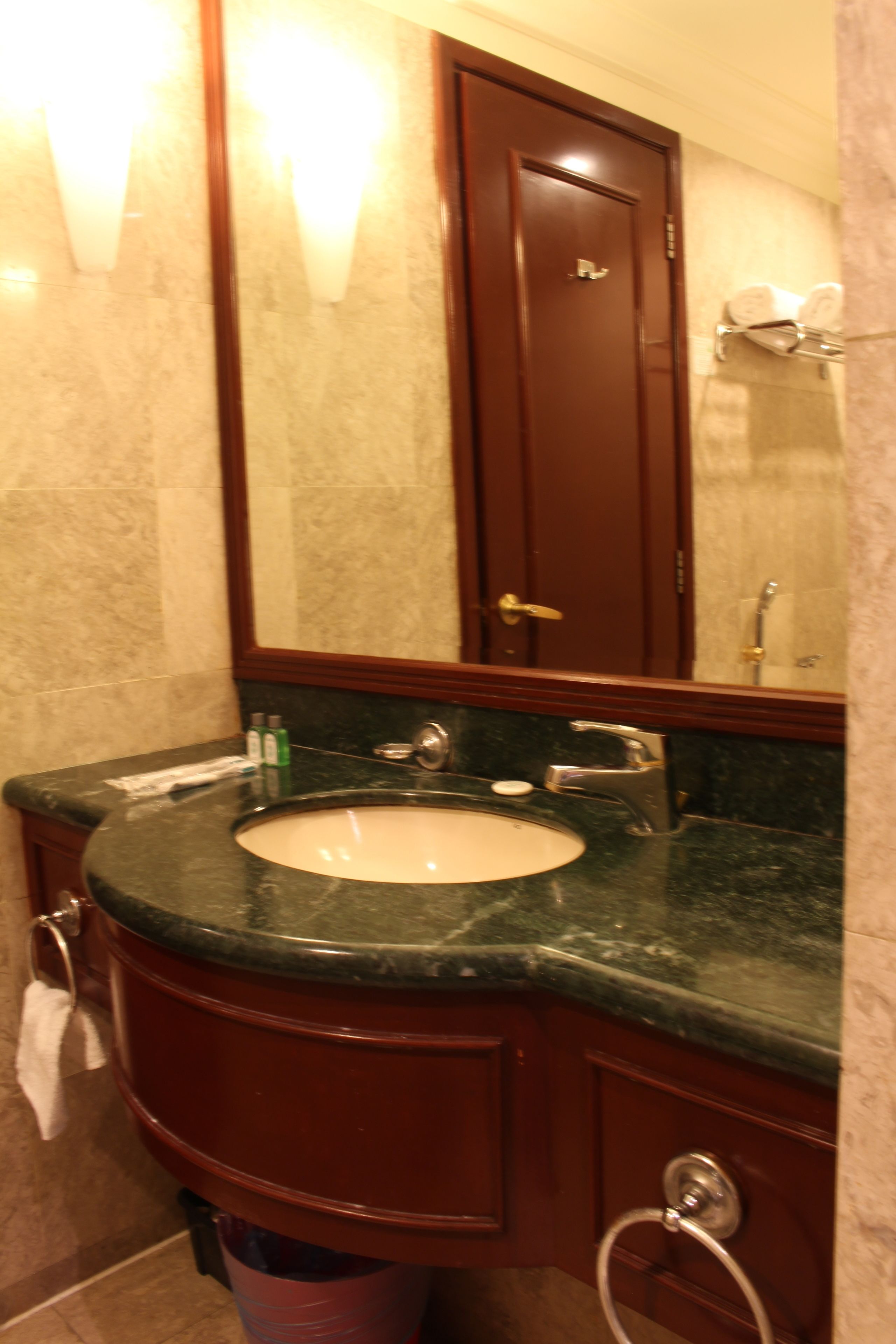 A bathroom with a marble sink, a mirror, a towel rack, and a door.