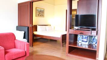 A hotel room with a bed, a TV on a wooden stand, a red armchair, and a painting on the wall.