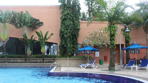 A swimming pool with lounge chairs and umbrellas, surrounded by greenery and a building with a peach-colored exterior. - Grand Service Suite at Times Square (Kuala Lumpur)