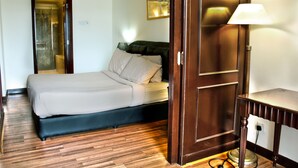A hotel room with a bed, a wooden floor, a desk with a lamp, and a painting on the wall. - Grand Service Suite at Times Square (Kuala Lumpur)