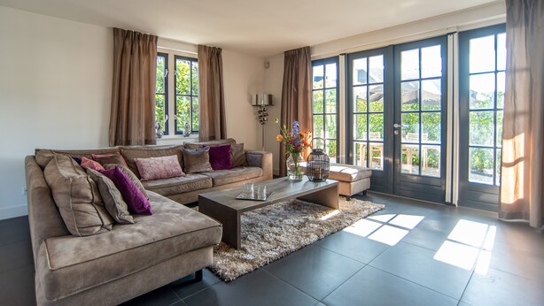 A modern living room with a sectional sofa, a coffee table, and large windows with curtains. - Najade Resort (Loosdrecht)