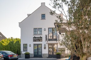 A white building with a sign reading "NAJADE Resort" and a reception area. There are two black doors, a balcony with a railing, and a car parked in front.