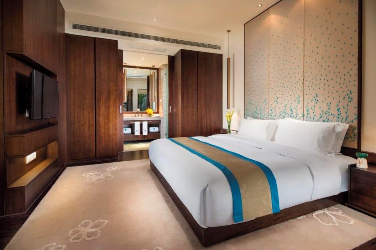 A modern hotel room with a large bed, wooden wardrobe, and a flat-screen TV.