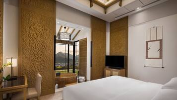 A hotel room with a large bed, a desk with a chair, a television, and a view of mountains through a large window.