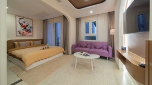 A modern hotel room with a large bed, a purple sofa, a white coffee table, and a TV mounted on the wall. - Pavillon Garden Hotel & Spa (Nha Trang)