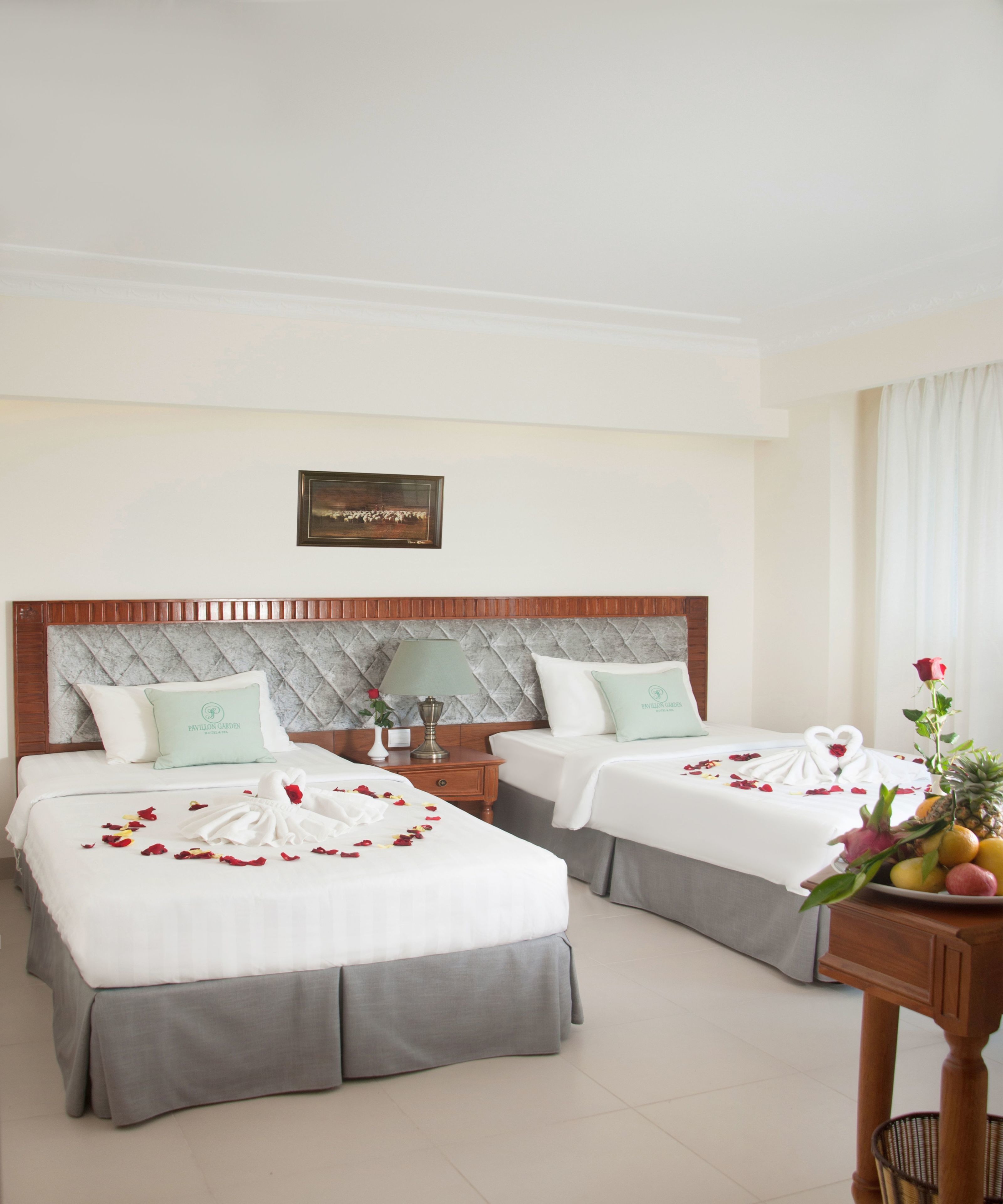 Una habitación de hotel con dos camas, cada una con una almohada y una mesita de noche. Hay un letrero en la pared y un jarrón con flores sobre una mesa.