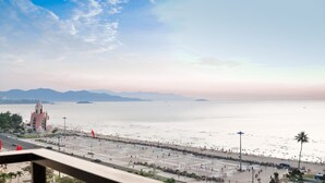 A coastal cityscape with a large public square, a prominent building with a unique architectural design, and a calm sea with distant mountains. - Pavillon Garden Hotel & Spa (Nha Trang)