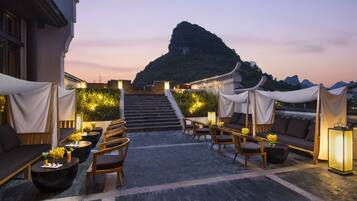 A rooftop terrace with outdoor seating, a staircase leading to a mountain, and ambient lighting.