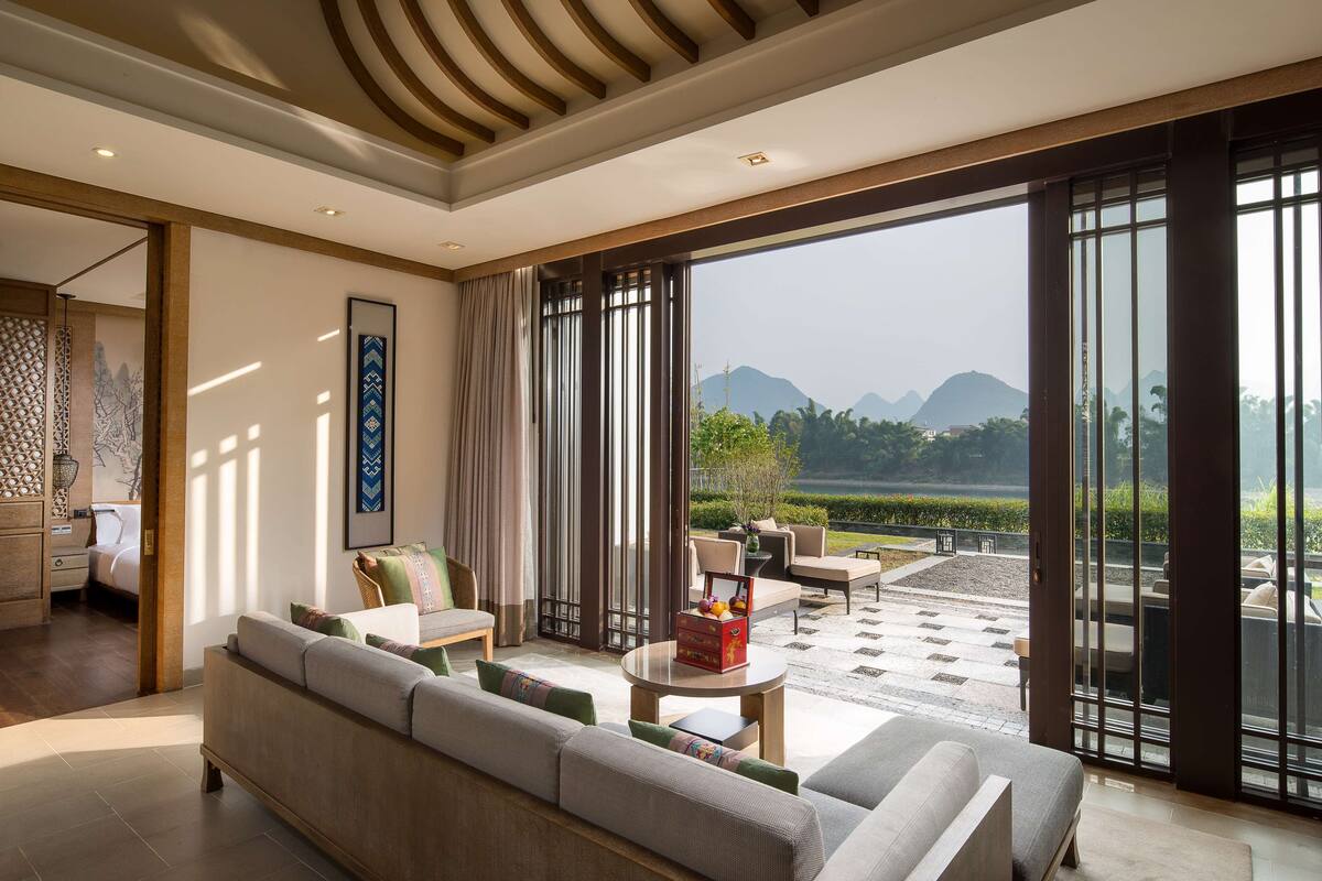 A modern living room with a sofa, coffee table, and a view of a garden and mountains.
