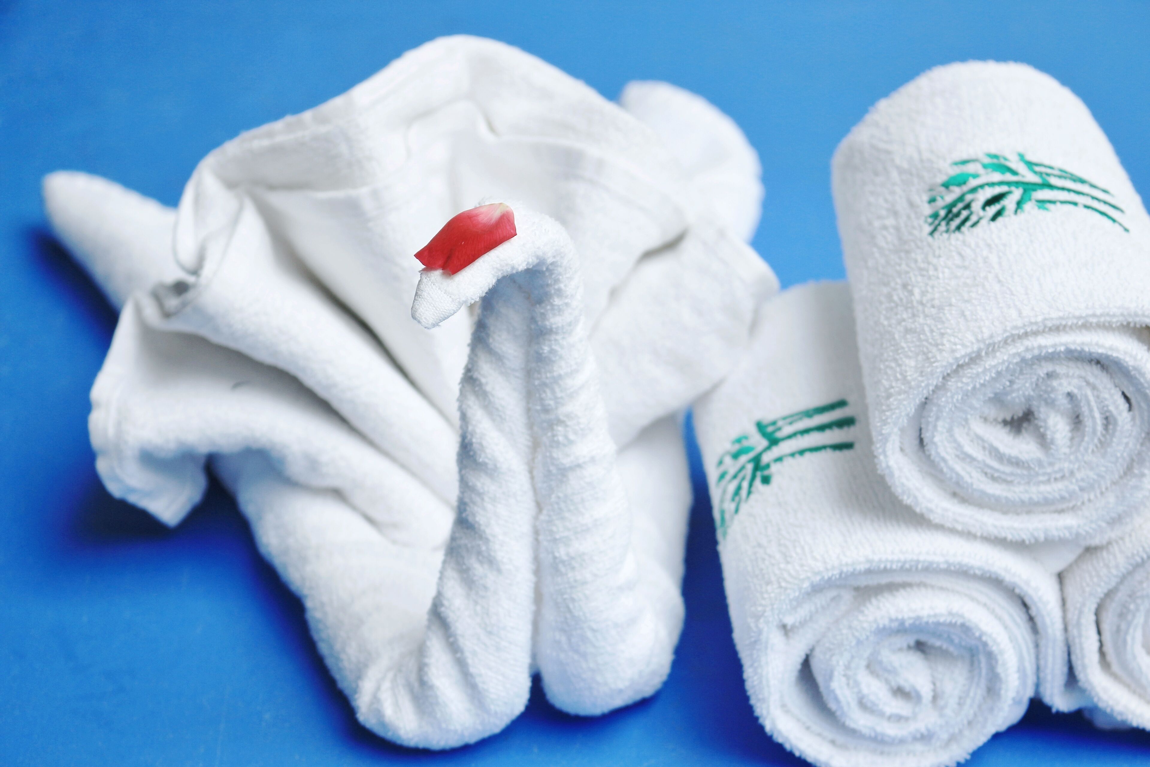 A swan-shaped towel with a red tag and rolled towels with green leaf patterns.