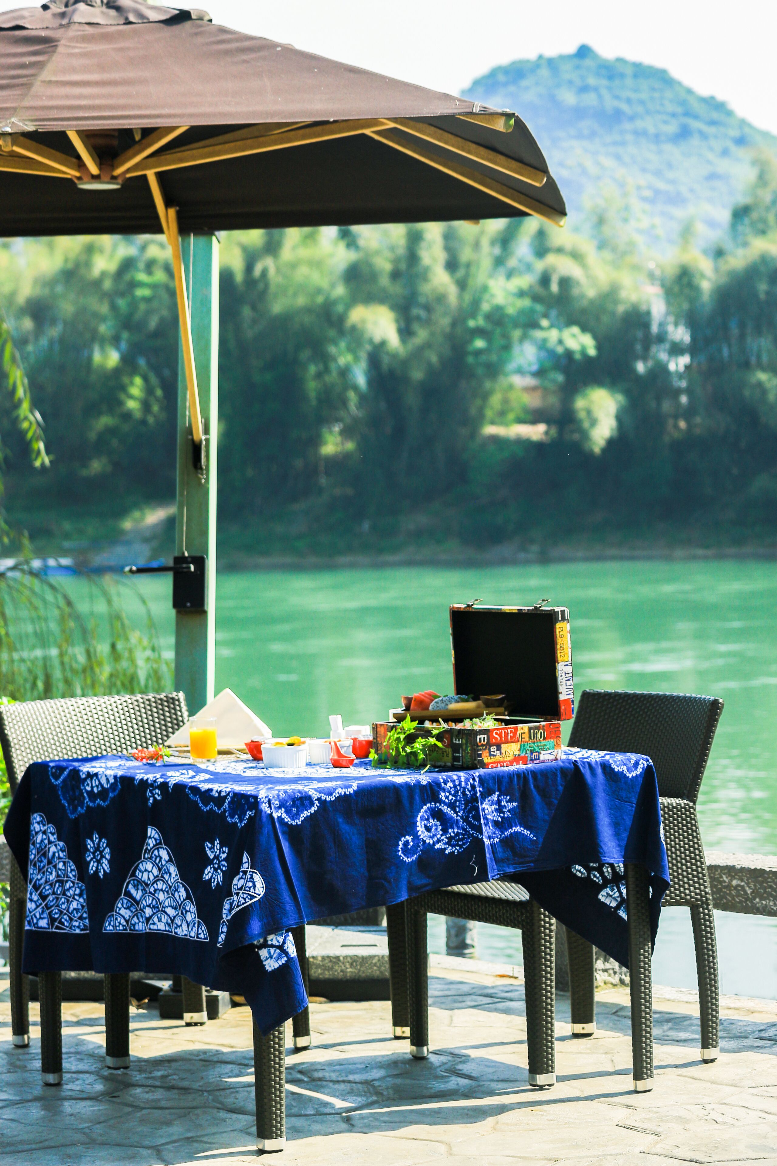An outdoor dining area with a table covered in a blue tablecloth, chairs, and an umbrella.