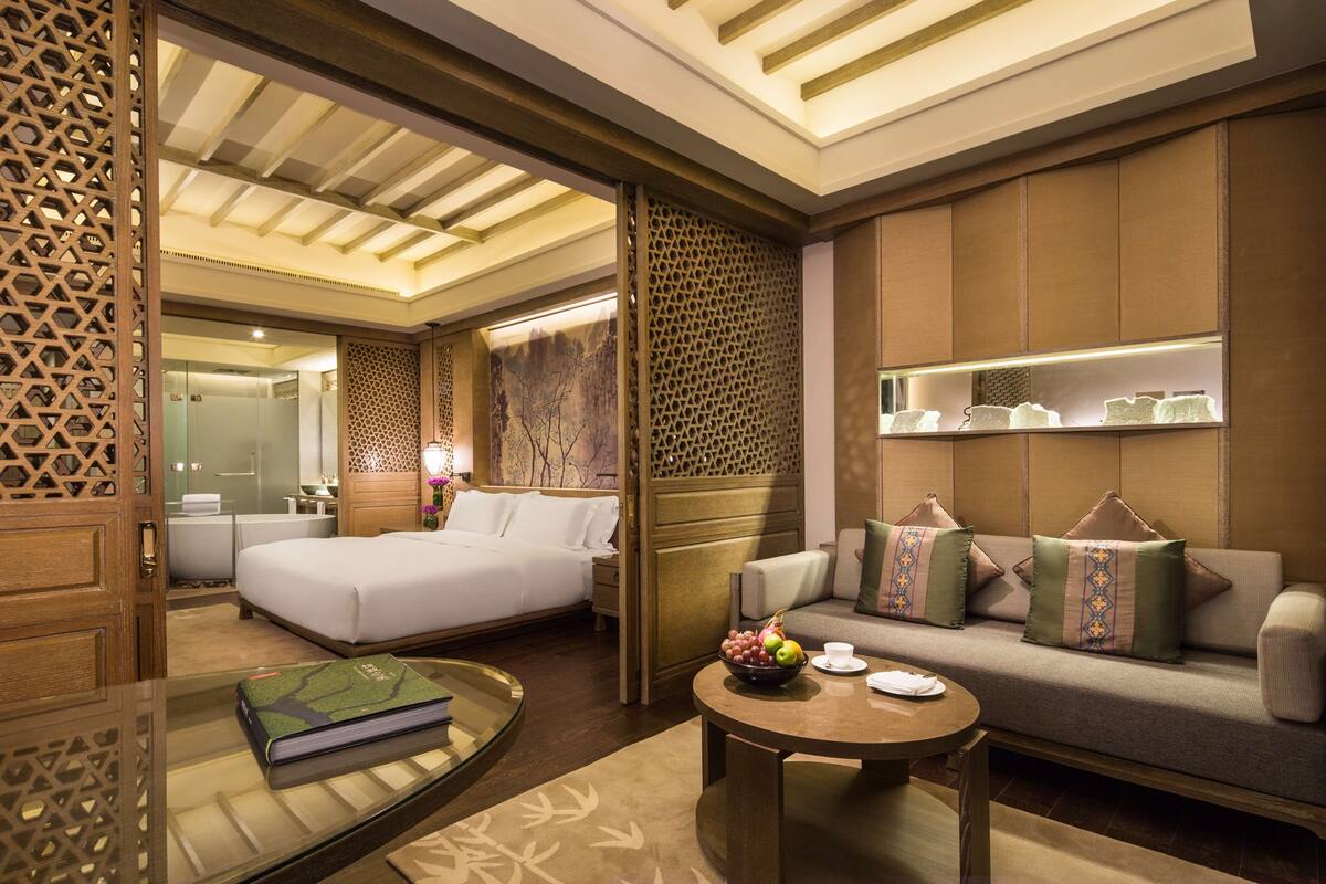A hotel room with a bed, a sofa, a coffee table, and a decorative wall.