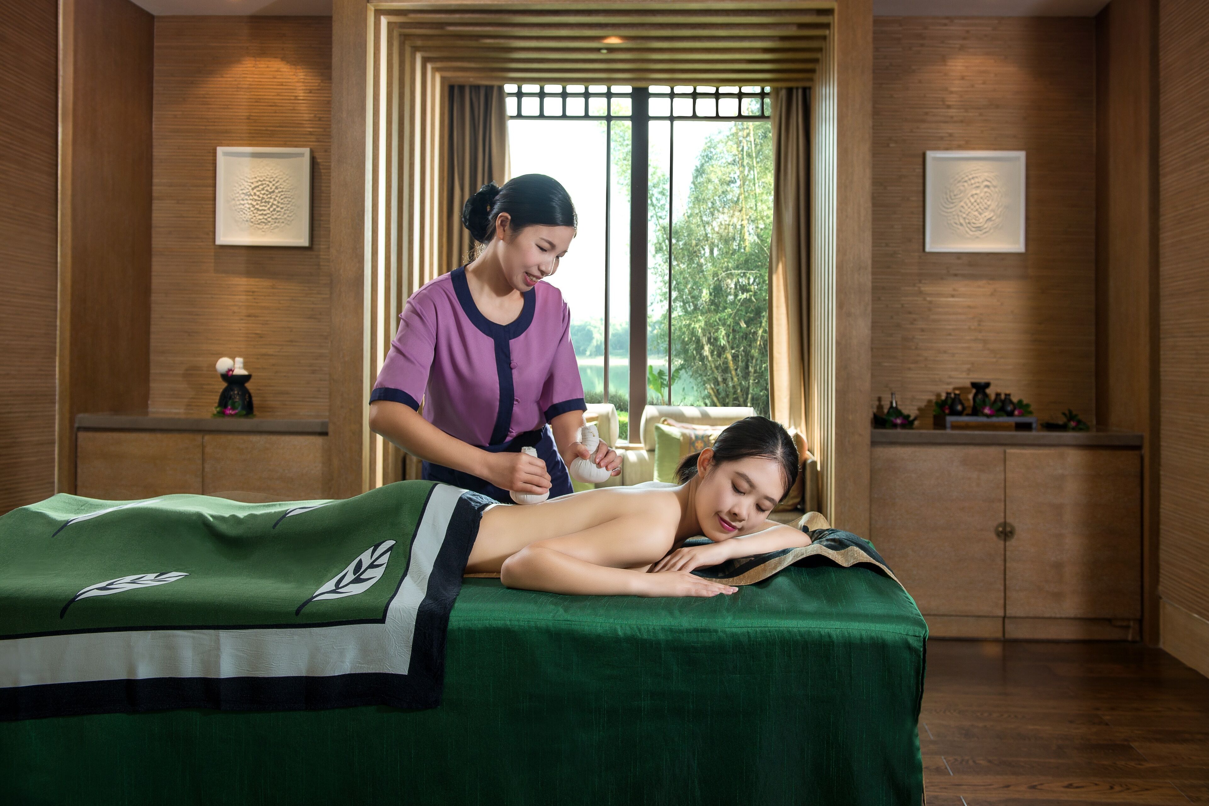 A massage therapy room with a wooden interior, a massage table, and a window with a view of greenery.
