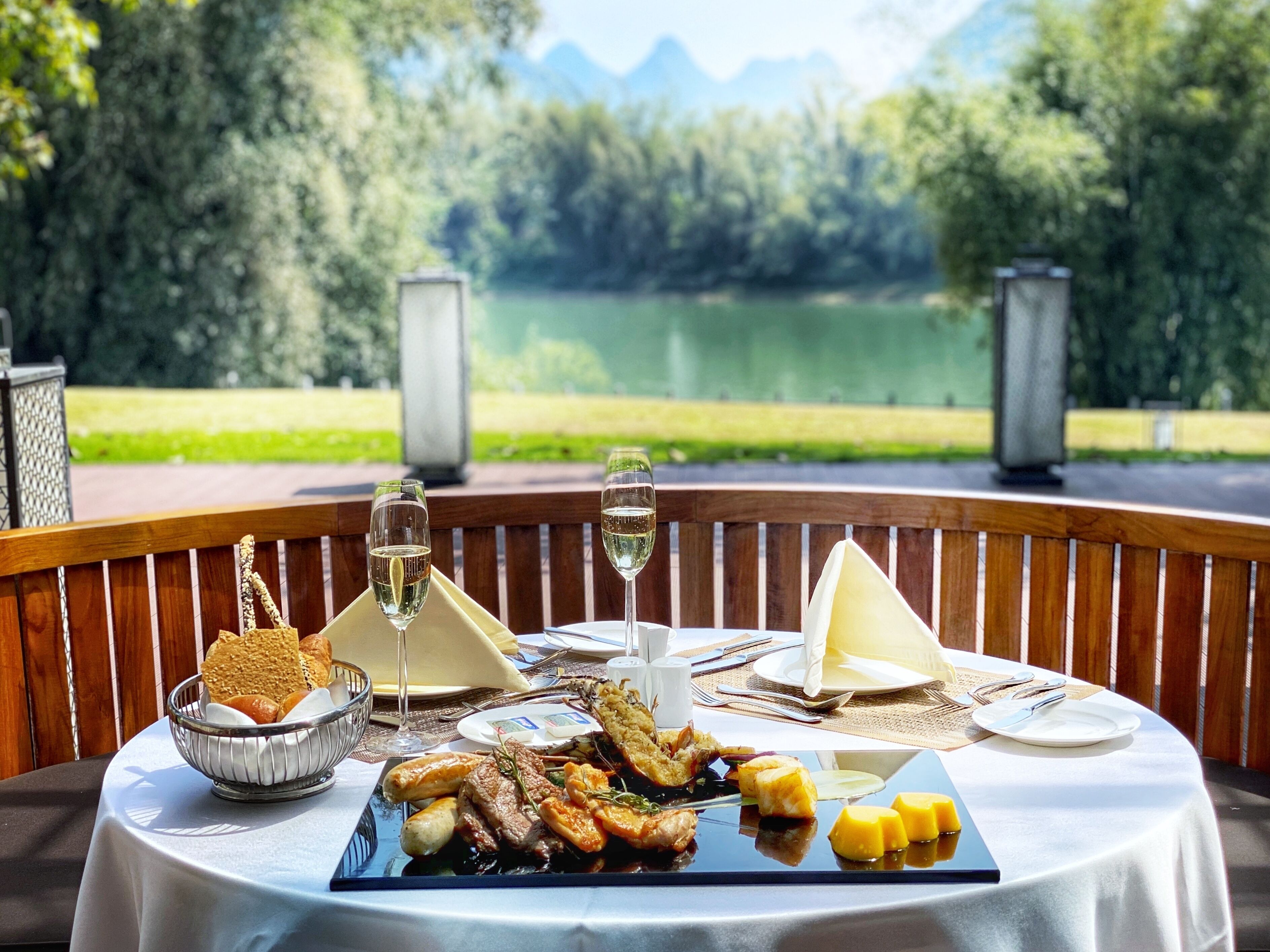 Une table dressée pour un repas, avec une vue pittoresque sur un lac, comprenant une variété de plats et des verres de vin.