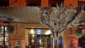 A hotel entrance with a large, sculptural tree in the foreground, a modern building facade, and a sign reading "SAIF SUITES". - Saifi Suites Hotel (Beirut)