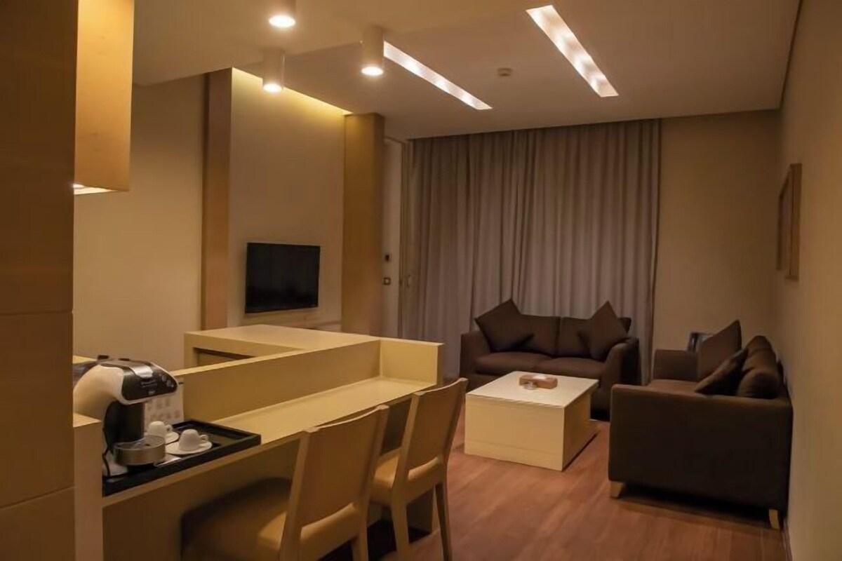 Habitación de hotel moderna con televisor de pantalla plana, sofá, mesa de centro y escritorio con cafetera.