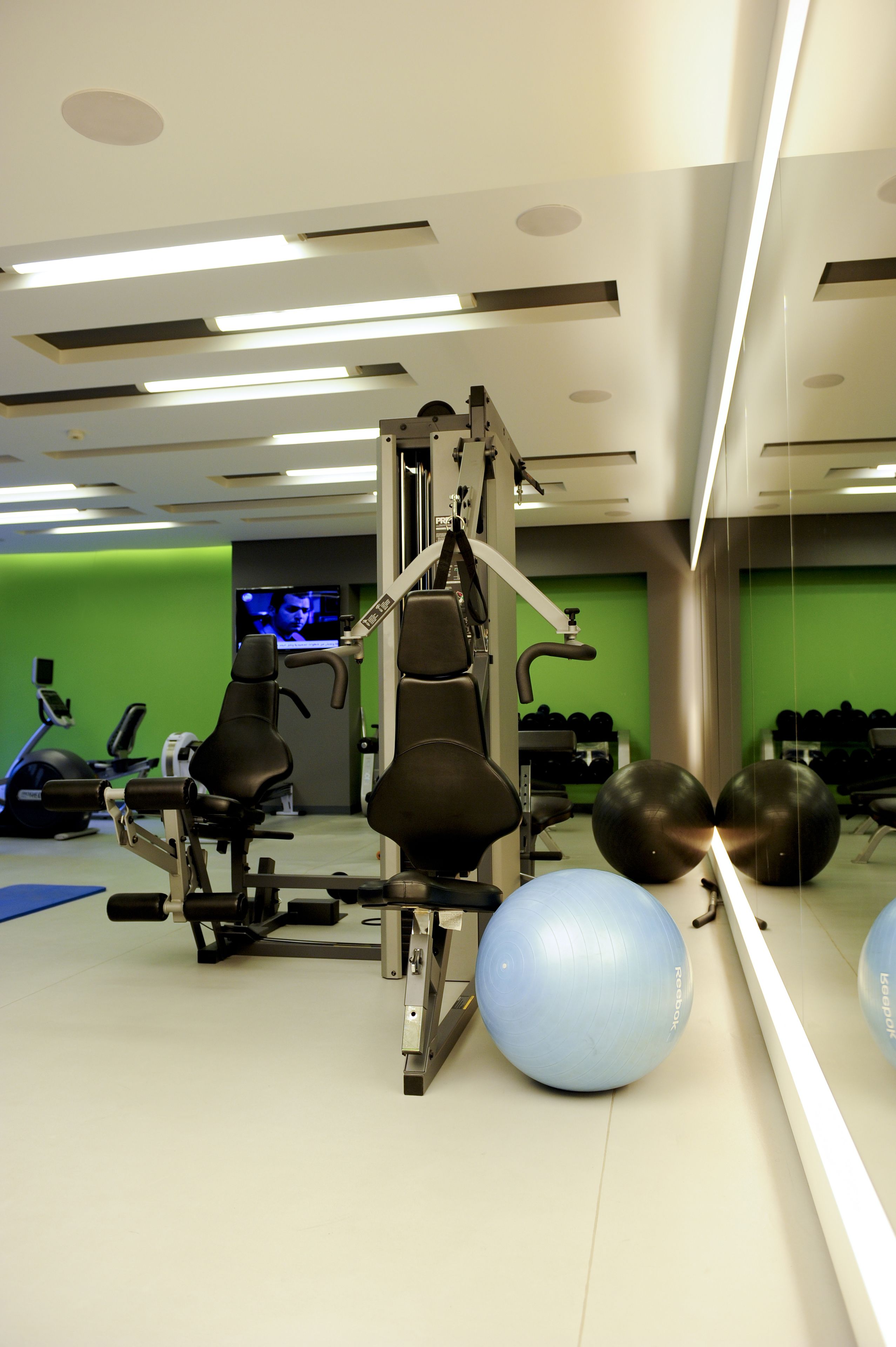 A gym with exercise equipment, a mirror, and a green wall.