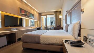 A modern hotel room with a large bed, a desk, a flat-screen TV, and a city view.