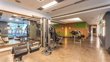 Un gimnasio con máquinas de cardio, equipo de pesas y un espejo grande.