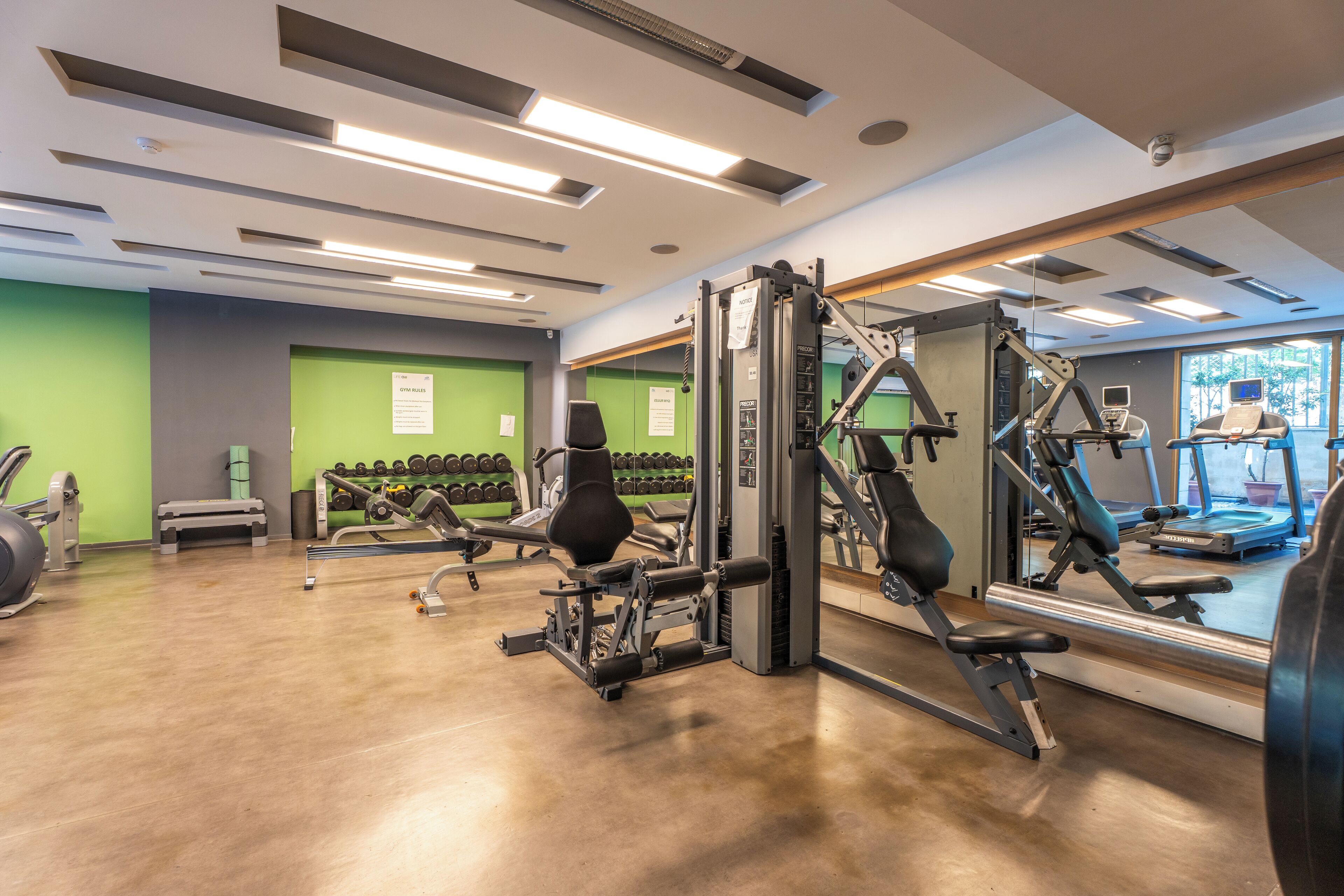 Ett gym med träningsutrustning, en spegel och en grön vägg.